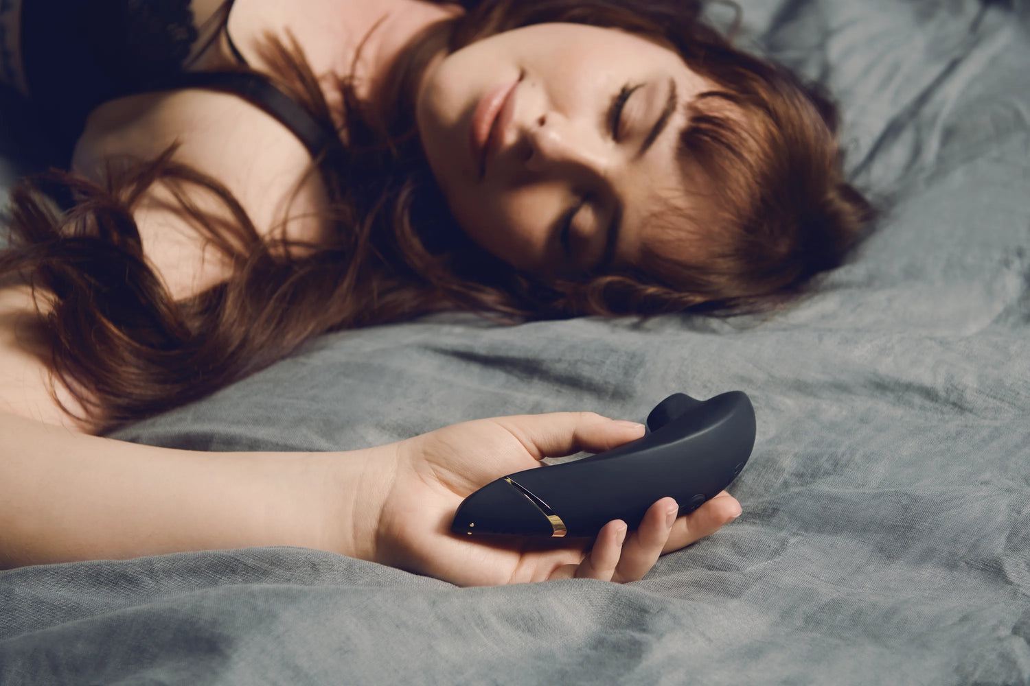 Afslappet kvinde hviler med Womanizer Premium 2 i hånden – et stilfuldt og diskret intimprodukt til dyb nydelse. Sensuel stemning skabt af Nevola med levering i hele Danmark.