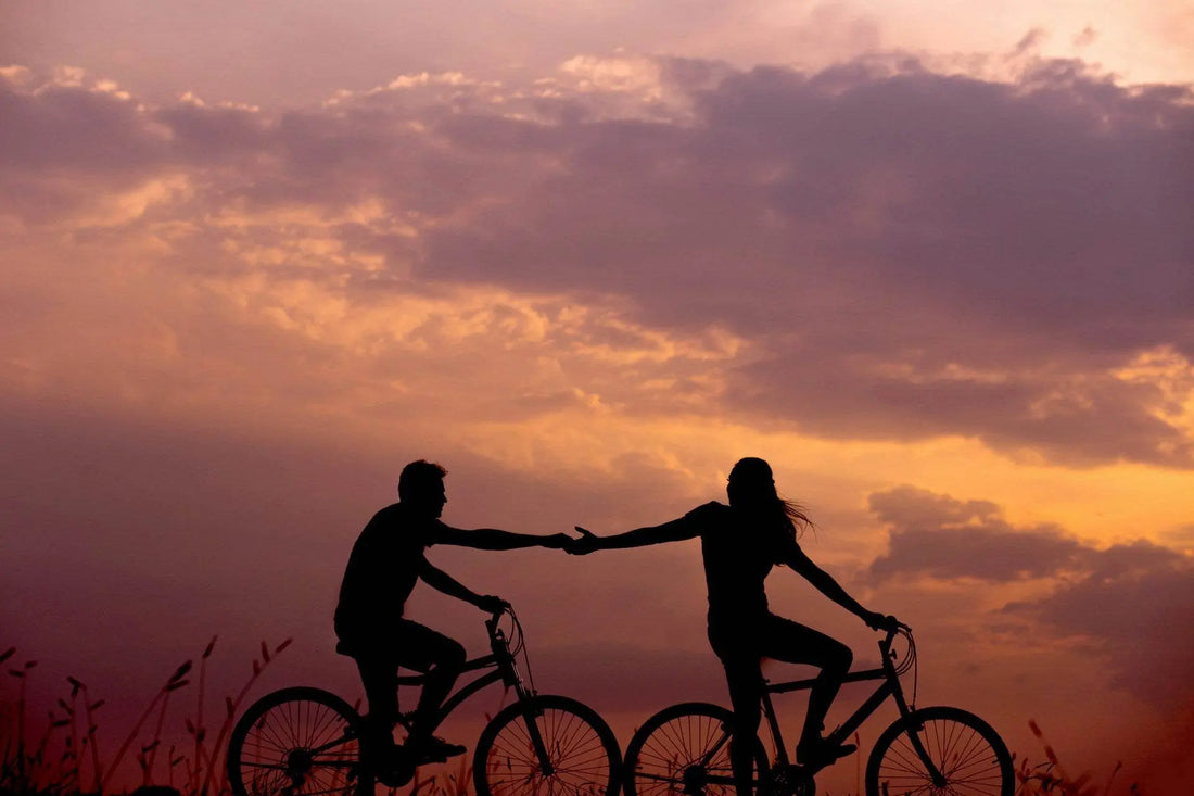 Et romantisk øjeblik ved solnedgang, hvor et par cykler side om side og holder i hånd. Ideel stemning til wellness, kærlighed og nærvær. Perfekt til branding af sanselig livsstil.