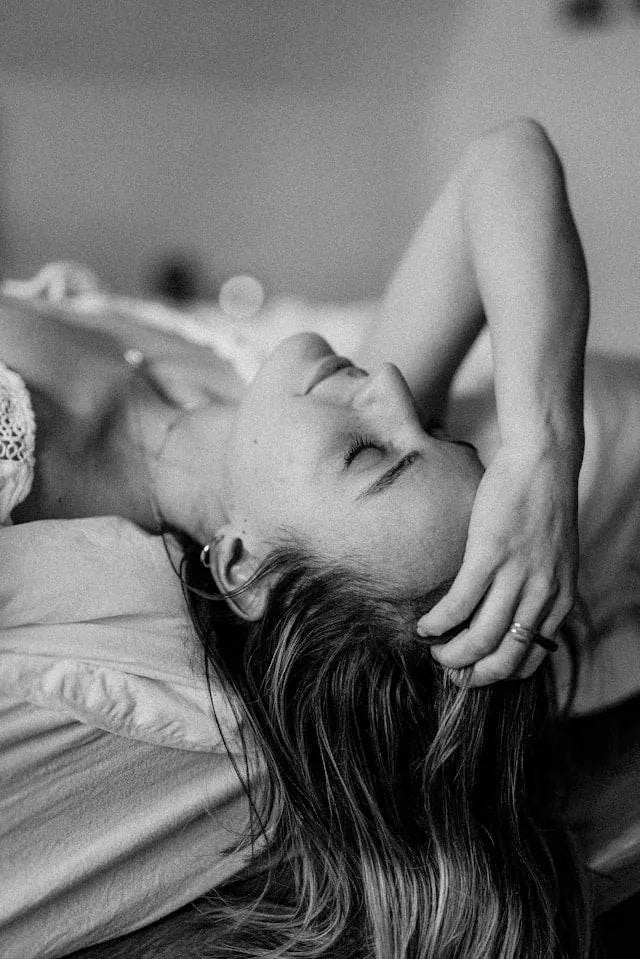 Kvinde i blødt lingeri ligger afslappet på sengen og nyder et øjebliks stilhed og sanselig ro – et æstetisk billede, der symboliserer moderne intim wellness og selvforkælelse.