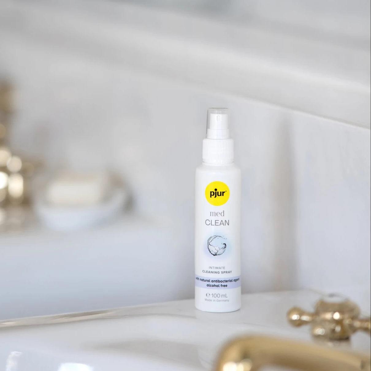Pjur Med Clean rengøringsspray placeret elegant på badeværelse med gyldne detaljer. Lifestyle-billede der viser diskret og stilfuld pleje af intimprodukter i en rolig, naturlig hverdagsscene.