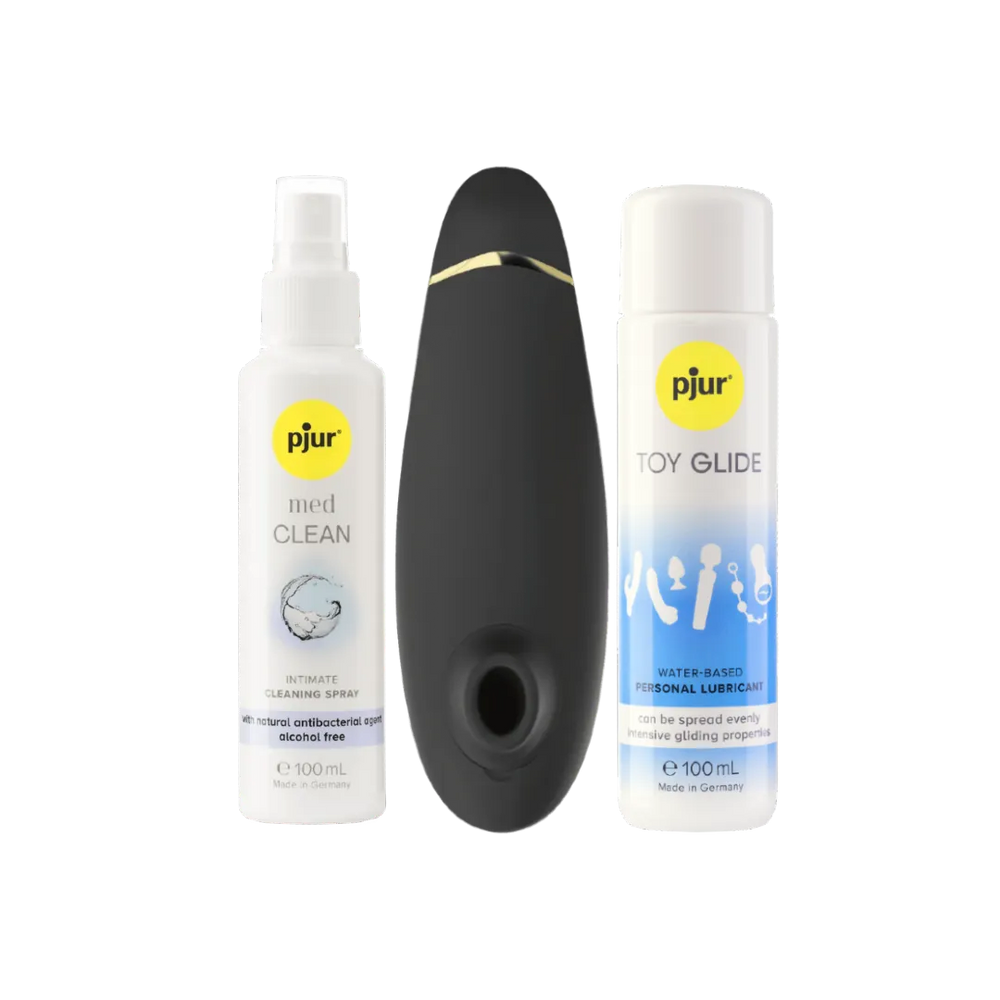 Womanizer Premium 2 lufttryksvibrator placeret mellem Pjur Toy Glide glidecreme og Pjur Med Clean rengøringsspray. Et komplet intimprodukt-sæt, der forener sanselig stimulering, plejende glideoplevelse og sikker rengøring til moderne erotisk wellness.
